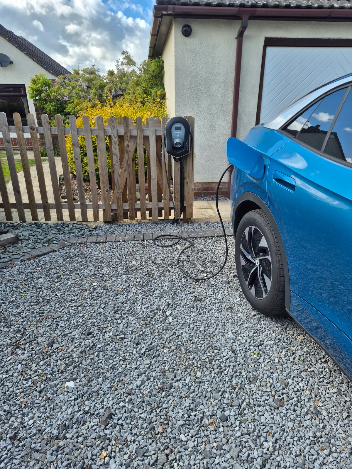 Myenergi Zappi charge point on a post beside a detached garage in Ringwood, with an electric car on charge on the gravel drive