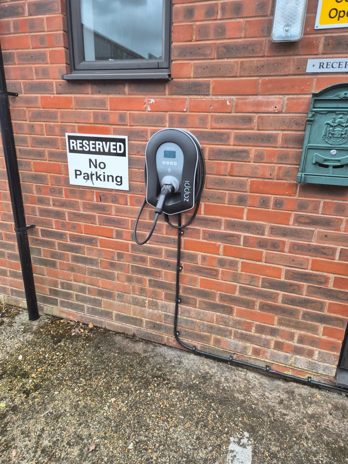 Myenergi Zappi 2 charge point on a brick wall at a Salisbury workplace, beside a reserved parking bay